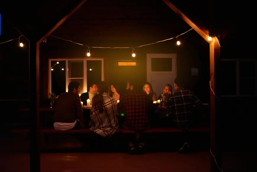 Grupa znajomych siedzi na tarasie w wieczór przy stole - ogrzewa ich promiennik podczerwieni